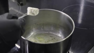 Eritilmiş tereyağına eritilmiş un eklemek paslanmaz çelik tencereye modern bir soba tepsisi, yemek pişirme sürecine eldiven ile yakın çekim