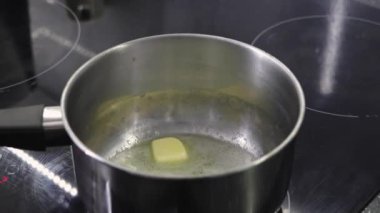 Modern bir fırının üzerinde paslanmaz çelik bir tencerede erimekte olan tereyağının yakın çekimi, pişirme sürecine odaklanmış bir şekilde.