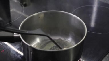 Modern bir sobanın üstünde tereyağını eritmek, yemek pişirme sürecine yakın çekim siyah bir spatula ile yavaşça karıştırmak.