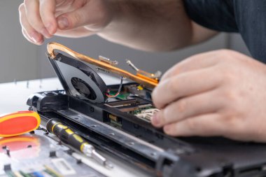 Bakım sırasında temizlik için bir dizüstü bilgisayar soğutma sisteminin kaldırılması, iç bileşenleri dikkatlice söken bir teknisyenin yakın plan çekimi