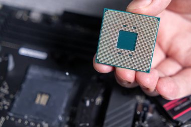 Arka planda bir anakart ile el ele tutulan bir işlemcinin yakın çekimi, altın raptiyeler ve teknik tasarım sergileniyor 