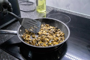 stirring sauted mushrooms and chicken in a skillet on a stovetop with a black spatula  clipart