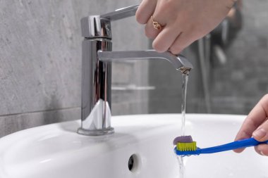 Lavabodaki bir diş fırçasına musluktan akan suyla fırçalama rutini