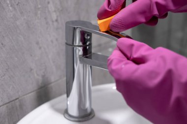 Krom banyo musluğunu süngerle temizlemek koruyucu eldiven giyerken.