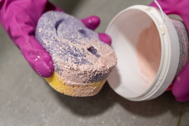 Eldivenli ellerle tutulan pembe macunlu temizlik süngeri, yüzey temizleme ve leke temizleme için hazır.