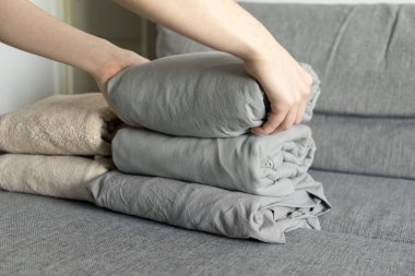 Gri çarşafları yumuşak kumaş kanepeye dizer, elleri dikkatlice katlanır yatakları düzenli ve düzenli bir şekilde düzenler.