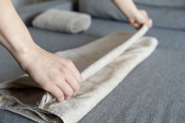 Gri bir kanepeye bej havluyu katlayan eller. Düzeni, düzenliliği ve temiz bir ev ortamını vurgulayan eller. 