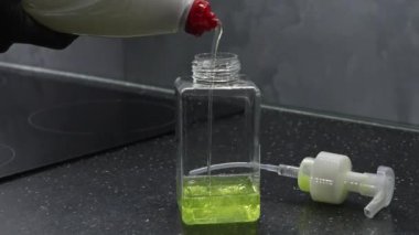 Karanlık bir mutfak tezgahında bulaşık deterjanı şişesine dökmek. Yakın çekim.