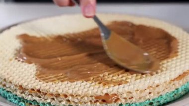 Karamelize edilmiş yoğunlaştırılmış sütü kaşık ile waffle tabakalarına yaymak, tatlı hazırlığını vurgulamak ve ev yapımı tatlı