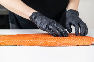 Şef taze somon filetosundaki balık kemiklerini beyaz mutfak yüzeyinde siyah eldiven kullanarak kontrol ediyor.