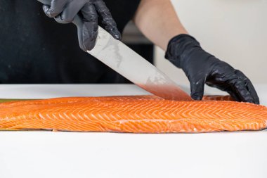 chef cutting fresh salmon fillet with precision using a sharp knife while wearing black gloves for safe and clean preparation clipart