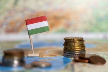Macar bayrağı dünya haritasında istiflenmiş sikkelerle ulusal ekonomiyi, finansal gelişimi ve uluslararası ekonomik bağlantıları temsil ediyor.