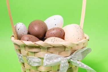 Benekli yumurtaların olduğu Paskalya sepeti kahverengi ve beyaz tonlarda parlak yeşil bir zemin üzerinde, benekli bir kurdele ile süslenmiş.