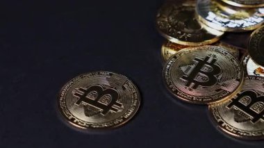 Parlak bitcoin paraları karanlık bir yüzeye saçılmış, ışığı yansıtıyor ve kripto para sembollerinin altın detaylarını vurguluyor.