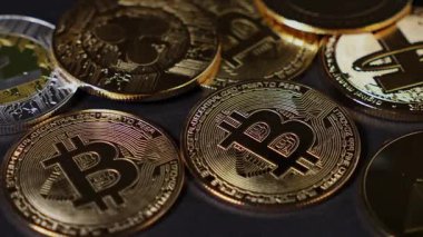 Parlak bitcoin paraları karanlık bir yüzeye saçılmış, ışığı yansıtıyor ve kripto para sembollerinin altın detaylarını vurguluyor.