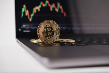Arkaplanda borsa grafiği, kripto para ticareti ve finansal konsepti olan dizüstü bilgisayardaki altın bitcoin.
