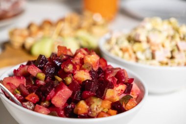 Pancar, patates, havuç, bezelye ve turşulu geleneksel sirkeli salata. Arka planda olivier salatası olan beyaz bir kâse.