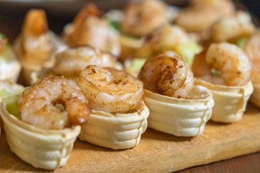 Krem peynirle doldurulmuş çıtır tartlar, taze salatalık ve ızgara karides, ahşap bir tahtada gurme aperatifi olarak servis edilir.