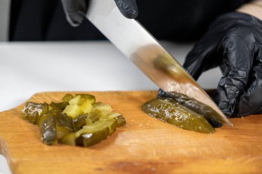 Tahtada turşu doğramak, şefin elleri siyah eldivenlerle yeşil bir salatalığı keskin bir bıçakla doğramak, salata hazırlığı.