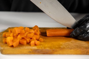 Salata hazırlamak için tahtadan küçük küplere haşlanmış havuç kesmek profesyonel bir mutfakta keskin bıçak kullanan siyah eldivenli şef.