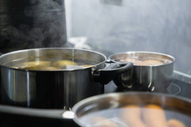 Fırında haşlanmış patates, yumurta ve havuçla birlikte üç tencere. Ev yapımı yemek hazırlığı için malzemeler pişerken buhar yükseliyor.
