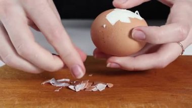 Salatalar, sandviçler ve ev yapımı yemekler için ahşap bir tahtanın üzerinde elle haşlanmış bir yumurtayı dikkatlice soyarken.