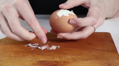 Haşlanmış yumurtayı ahşap bir tahtaya nazikçe soyarak taze salatalar, sandviçler ve ev yapımı yemekler için kabuk parçaları çıkararak.