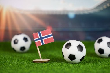  Yeşil çimlerin üzerinde ulusal bayrak ve stadyumdaki futbol toplarıyla Norveç futbol sahnesi tutku, takım çalışması ve spor mirasını temsil ediyor.