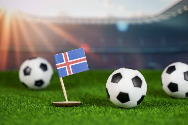 Ulusal bayrağı olan İzlanda futbol teması, yeşil çimlerde futbol topları, ve bulanık stadyum arka planı, spor tutkusunu, rekabeti ve ulusal gururu temsil ediyor.