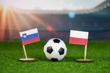 Slovenia, Polonya 'ya karşı milli bayraklar, yeşil sahada futbol topu ve stadyum, rekabeti, tutkuyu ve sportmenliği simgeliyor.