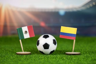 Meksika - Kolombiya futbol maçı konsepti ulusal bayraklar, yeşil sahada futbol topu ve bulanık stadyum arka planı.