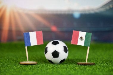 Fransa, Meksika 'ya karşı milli bayraklar, yeşil sahada futbol topu ve bulanık stadyum, uluslararası spor müsabakalarını ve rekabeti temsil ediyor.