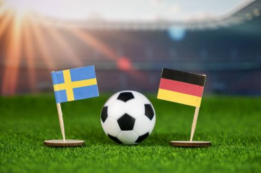 İsveç, Almanya 'ya karşı ulusal bayraklarla futbol maçı, yeşil sahada futbol topu ve uluslararası spor rekabetini temsil eden bulanık stadyum.