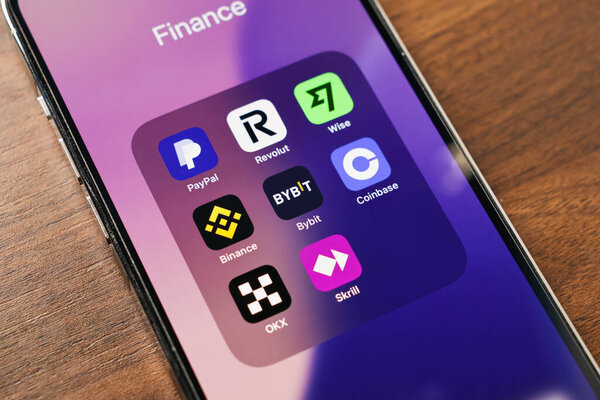 Познань, Польша - 12 марта 2025 года: крупный план экрана смартфона с популярными финансовыми приложениями, включая Paypal, revolut, wise, binance, coinbase, skrill, bybit и okx на фоне деревянного стола
