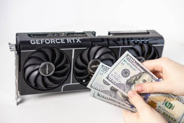 Poznan, Polonya - 28 Mart 2025: Asus GeForce RTX 5070 grafik kartının yanında Amerikan dolarlarını sayan kişi, modern oyun donanımının maliyetini gösteriyor