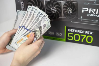 Poznan, Polonya - 28 Mart 2025: Asus GeForce RTX 5070 grafik kart kutusu önünde Amerikan dolarlarını sayan kişi, modern oyun donanımının yüksek fiyatını simgeliyor