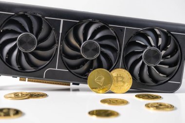 Beyaz bir yüzeye altın Bitcoin ve Ethereum paralarının yanına yerleştirilmiş güçlü üçlü fan grafik kartı. Kripto madenciliği ve engelleme teknolojisini resimleyen kavramsal resim