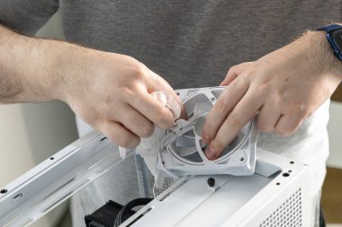 Bir teknisyen beyaz bir PC soğutma vantilatörünün pervanesini yumuşak bir bezle temizliyor. Vantilatör açık bilgisayar kutusunun üst panelinin üzerinde tutuluyor.