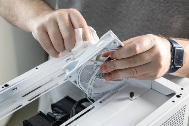 Bir teknisyen bilgisayar bakımı sırasında beyaz bir bilgisayar soğutma vantilatörünü bez ile temizliyor. Vantilatör, hava akımının verimliliğini sağlamak için davanın üst panelinden ayrıldı.