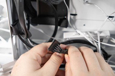 Bir teknisyen siyah bir SATA güç kablosunu bilgisayar kabinine bağlıyor. Görüntü, PC montajı veya iç donanım kurulumu sırasında yakın plan bir anı yakalar