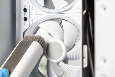 Bilgisayarın soğutma vantilatörünü temizlemek için yumuşak fırça kullanan bir teknisyenin yakın çekimi. Detaylı olay yeri dikkatli toz kaldırma ve bakımını vurguluyor.