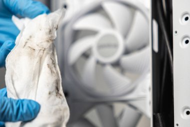 Mavi eldiven giyen bir teknisyen, bilgisayar çantasının içindeki beyaz soğutma vantilatörünün önünde kirli bir temizlik bezi tutuyor.