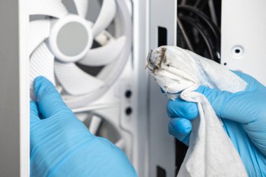 Mavi eldiven giyen bir teknisyen, beyaz bir bilgisayar kutusunun içinde tozlu bir soğutma vantilatörünü temizlerken kirli bir bez tutuyor. Görüntü uygulamalı bakımı gösteriyor