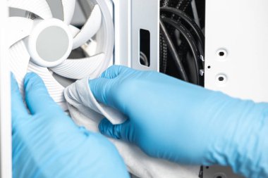 Mavi eldiven giyen bir teknisyen bir bez kullanarak beyaz soğutma vantilatörünü bir bilgisayar kutusunun içine dikkatlice siliyor. Olay yeri detaylı temizlik ve bakım işlerini gösteriyor.