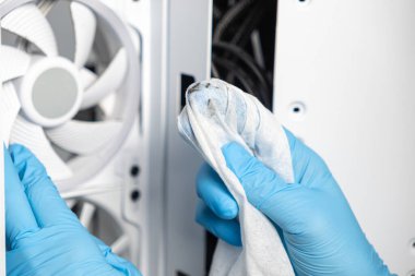 Mavi eldiven giyen bir teknisyen kirli beyaz bir bezle bir bilgisayar kutusunun içini temizliyor. Bir soğutma vantilatörü görünür, bir bakım süreci gösterir