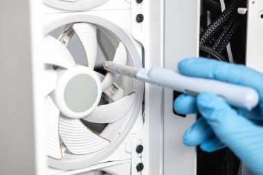 Mavi eldiven giyen bir teknisyen, beyaz bir bilgisayar çantasının içindeki tozlu bir soğutma vantilatörünü fırça kullanarak temizliyor. Olay yeri bakım ve bakımı vurguluyor