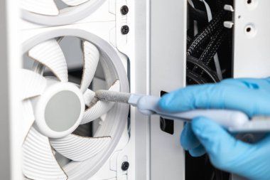 Bilgisayar çantasının içindeki kirli soğutma vantilatörünün tozunu temizlemek için yumuşak fırça kullanan mavi eldivenli bir teknisyenin yakın çekimi. Bilgisayar temizliği ve bakımı kavramı.