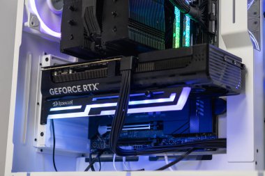 Poznan, Polonya - 30 Mart 2025: GeForce RTX GPU 'nun yan görüntüsü beyaz bir oyun bilgisayarına yüklendi. Grafik kartı sarkmayı önleyen ve modern bir görünüm ekleyen RGB ışıklandırmalı bir parantez tarafından destekleniyor
