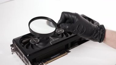 Poznan, Polonya - 27 Mart 2025: Beyaz bir yüzey üzerindeki ASUS GeForce RTX grafik kartının soğutma vantilatörünü incelemek için büyüteç kullanan siyah eldiven giyen bir kişinin yakın çekimi