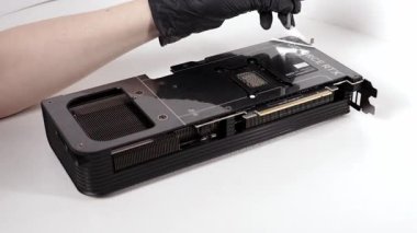 Poznan, Polonya - 27 Mart 2025: Bir kişi, temiz beyaz bir yüzey üzerindeki kutunun açılması sırasında bir ASUS GeForce RTX grafik kartının metal arka plakasındaki şeffaf koruyucu filmi dikkatlice kaldırdı